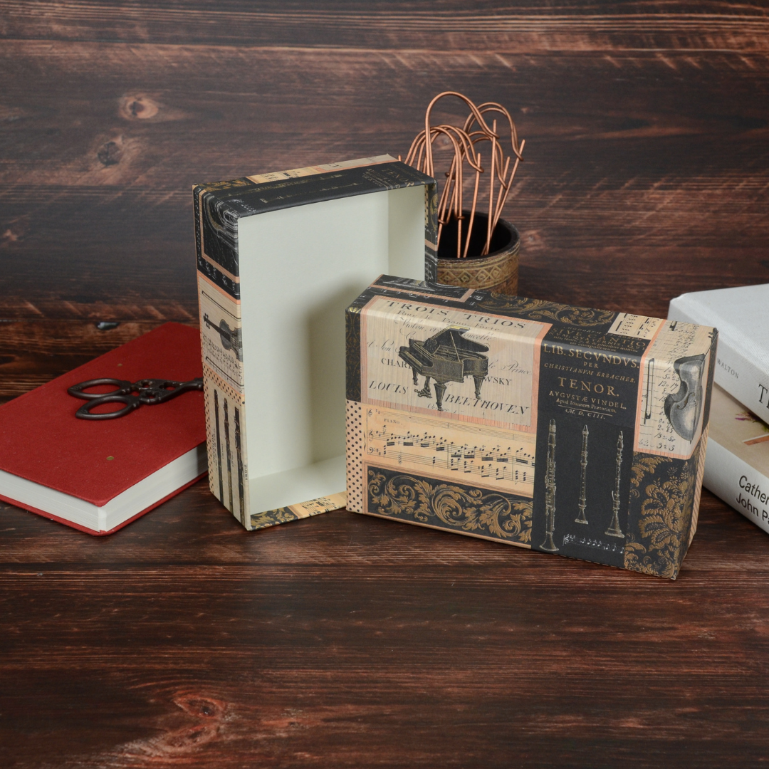 Melodia柄の文具箱を開けて中の小物を見せたイメージカット。周囲に本や筆記具を配置