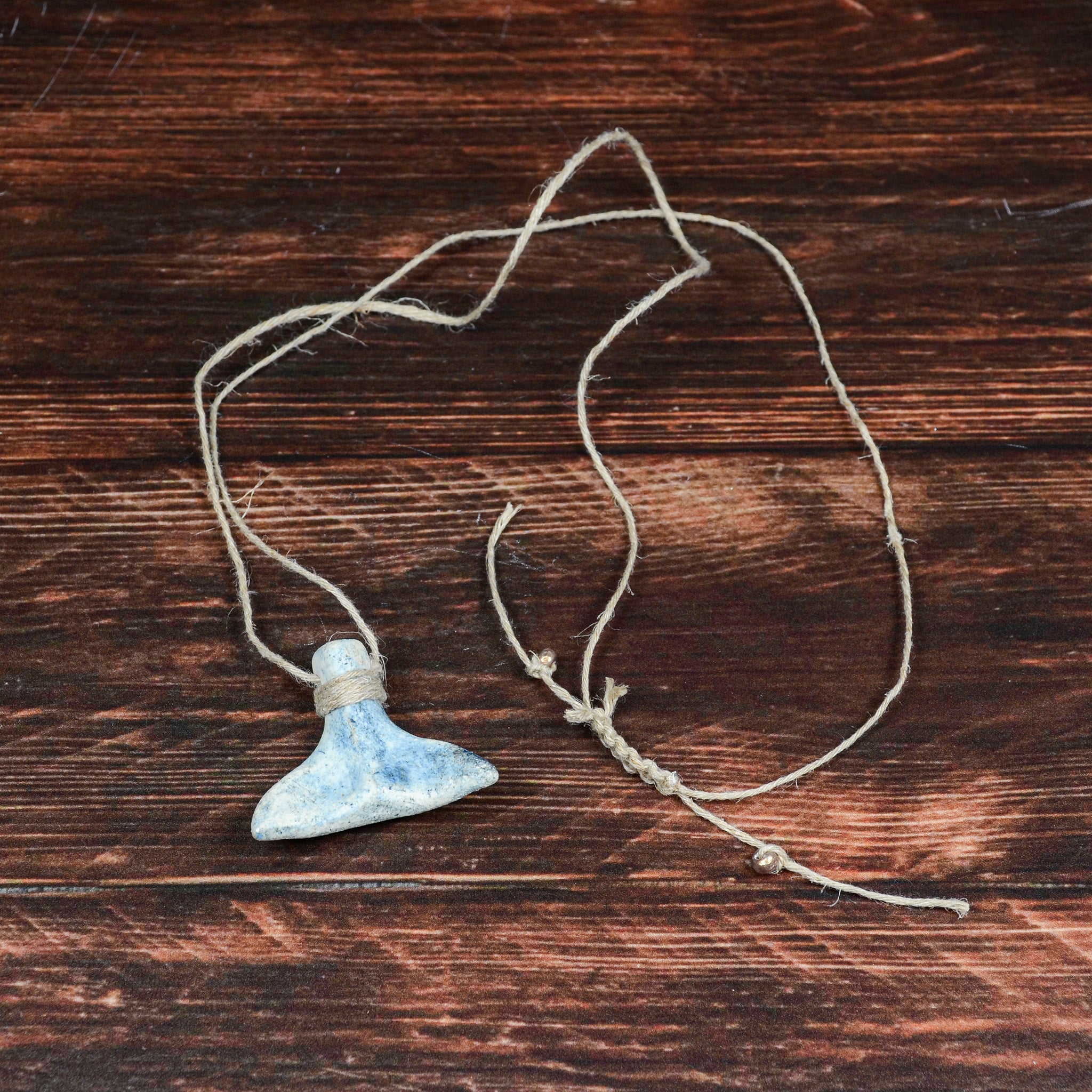 木目の上に置かれた「くじらのしっぽ」青。自然な釉薬のゆらぎと土の風合いが魅力の陶器チャーム。