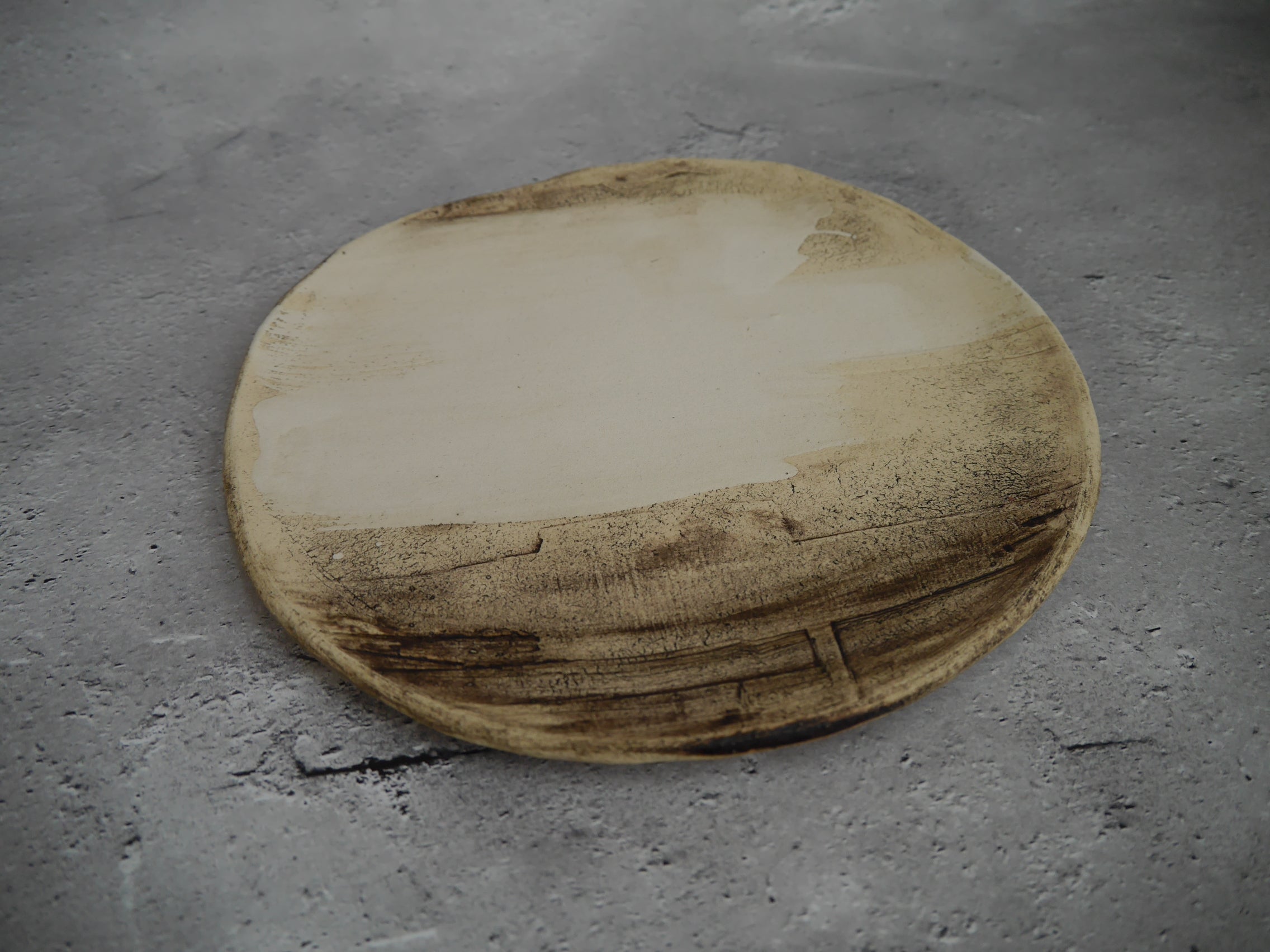 自然光のもとに置かれた陶器のプレート「Earth」。素朴であたたかみのある質感が特徴。