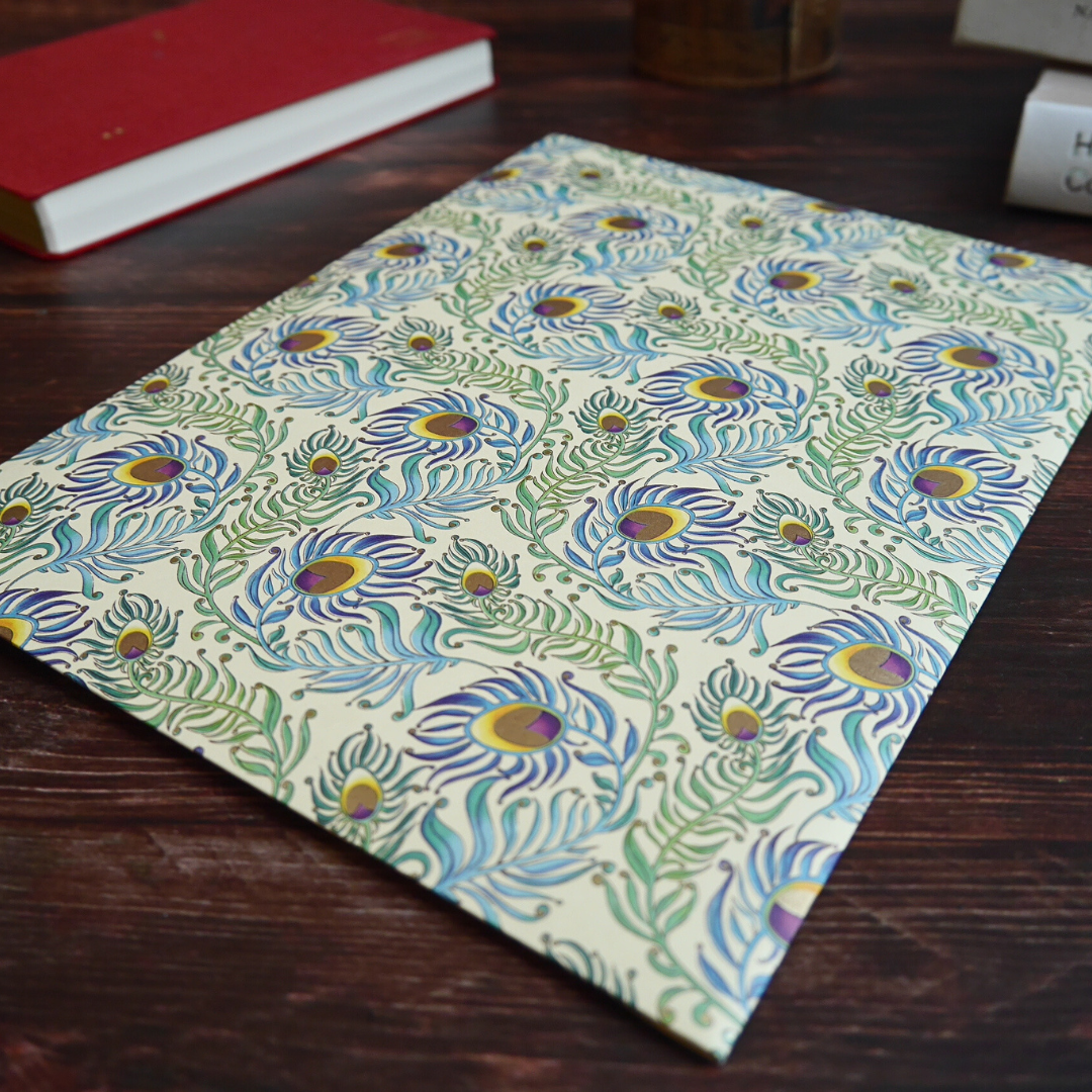 木のテーブルに置かれたPeacock柄のレターセット。羽模様と金粉印刷が柔らかく光を受けて輝く。