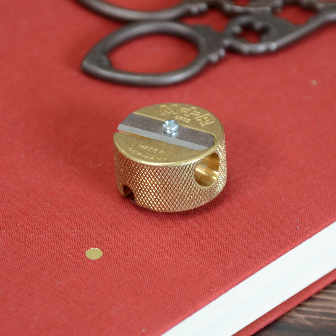 赤いノートと文房具と一緒に置かれた鉛筆削り。日常の使用シーンを想起させるスタイリング写真