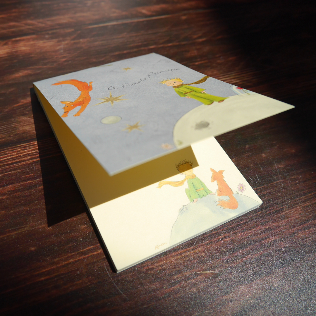 木目の机の上に置かれたKartosメモ。金粉が光を受けてきらめき、『星の王子さま』の世界が浮かび上がる。