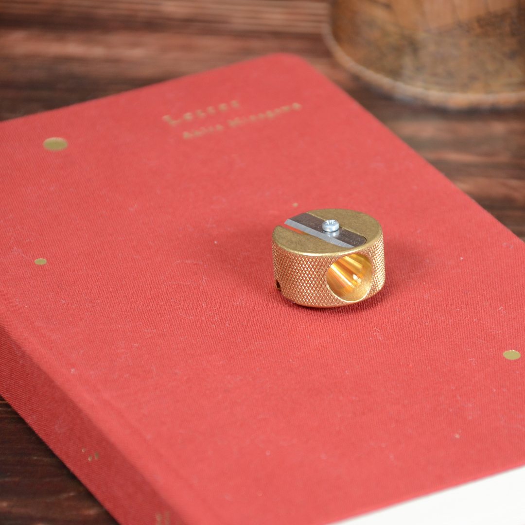 ノートの上に鉛筆削りが載った写真。手触り感と重厚な真鍮の素材感が伝わる構図