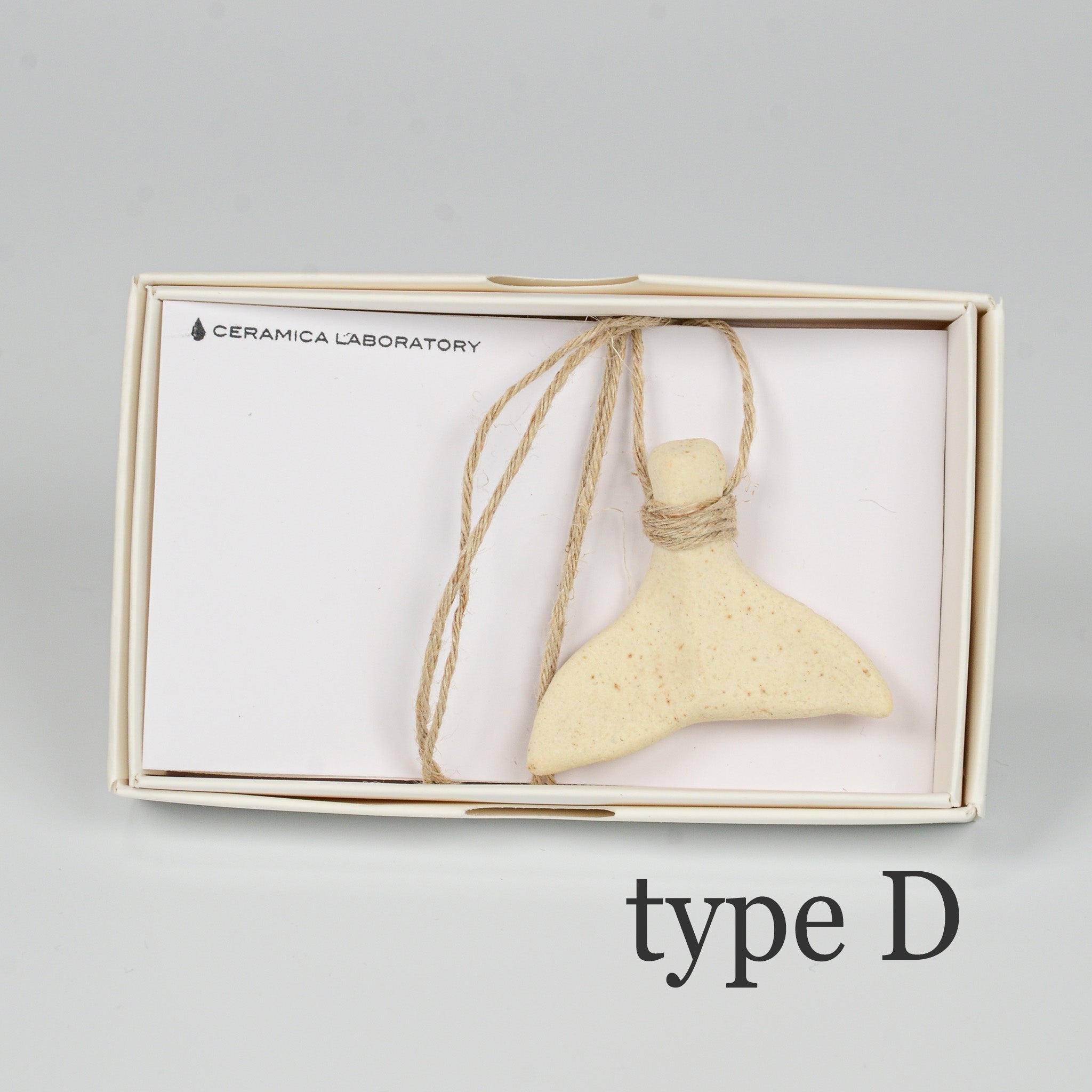 くじらのしっぽ「type D」。明るいベージュ系の色味で、静かな存在感を放つ陶器のチャーム。